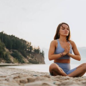 Woman practicing yoga meditation on a serene beach morning, promoting wellness.